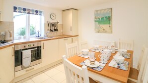 A kitchen with white cabinets, a wooden countertop, and a dining table set with white chairs and polka-dotted tableware. - Lobster Cottage (Weymouth)