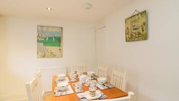 A dining area with a wooden table set for four, white chairs, and a beach-themed painting on the wall.