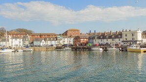 A harbor with boats docked, buildings along the waterfront, and a clear sky. - Lobster Cottage (Weymouth)