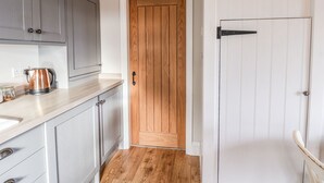 A narrow kitchen with grey cabinets, a wooden door, and a white door with a black handle. - The Stables (Scarborough)
