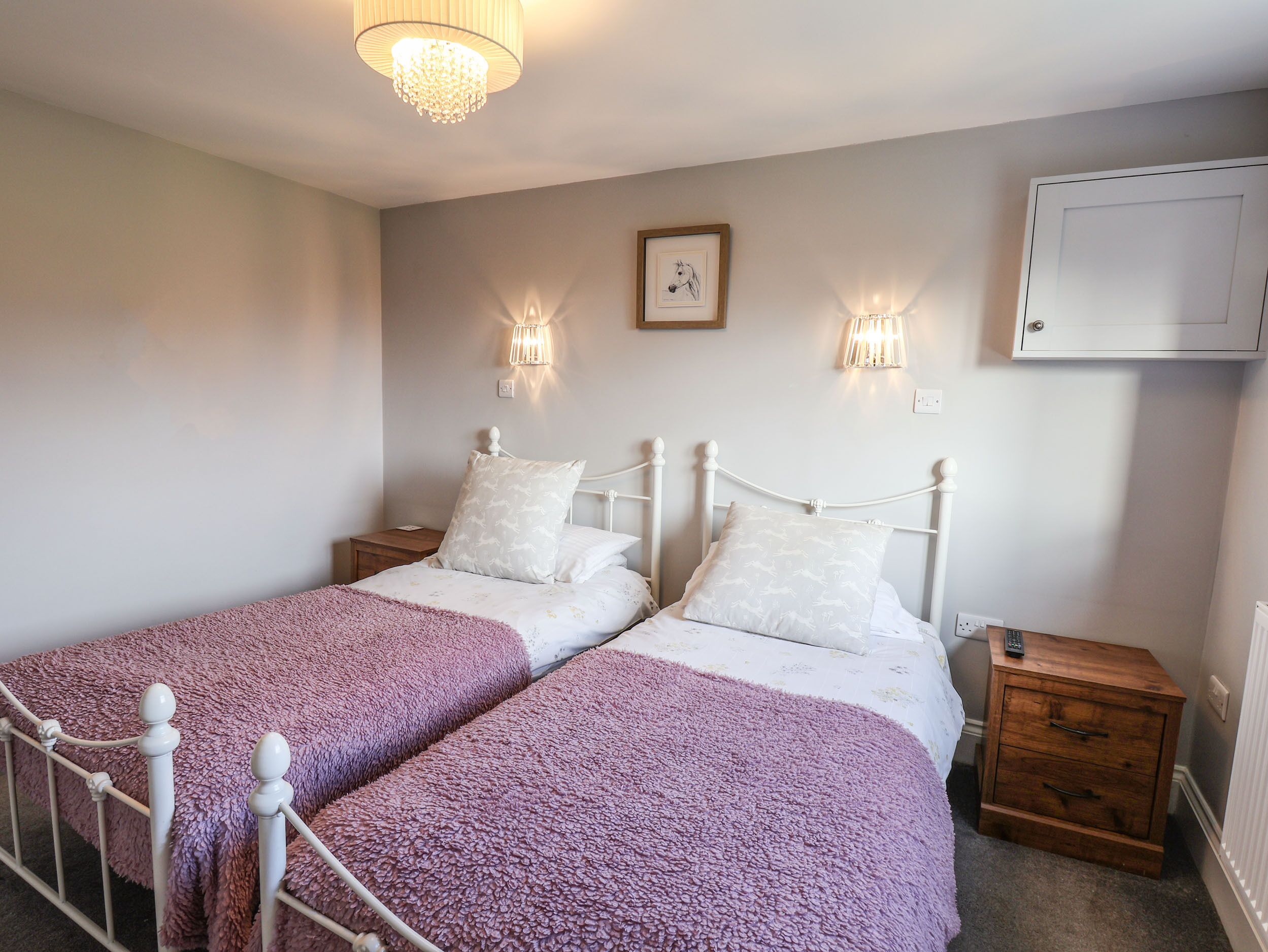 A bedroom with two beds, a wooden nightstand, a wall-mounted TV, and a chandelier.