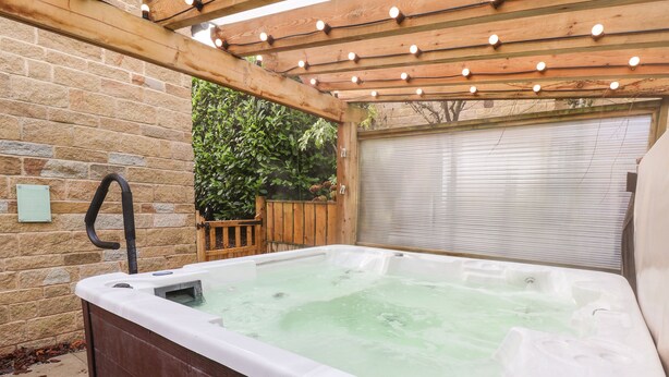 A hot tub with a wooden pergola overhead, a brick wall, and a wooden fence in the background. - The Stables (Scarborough)