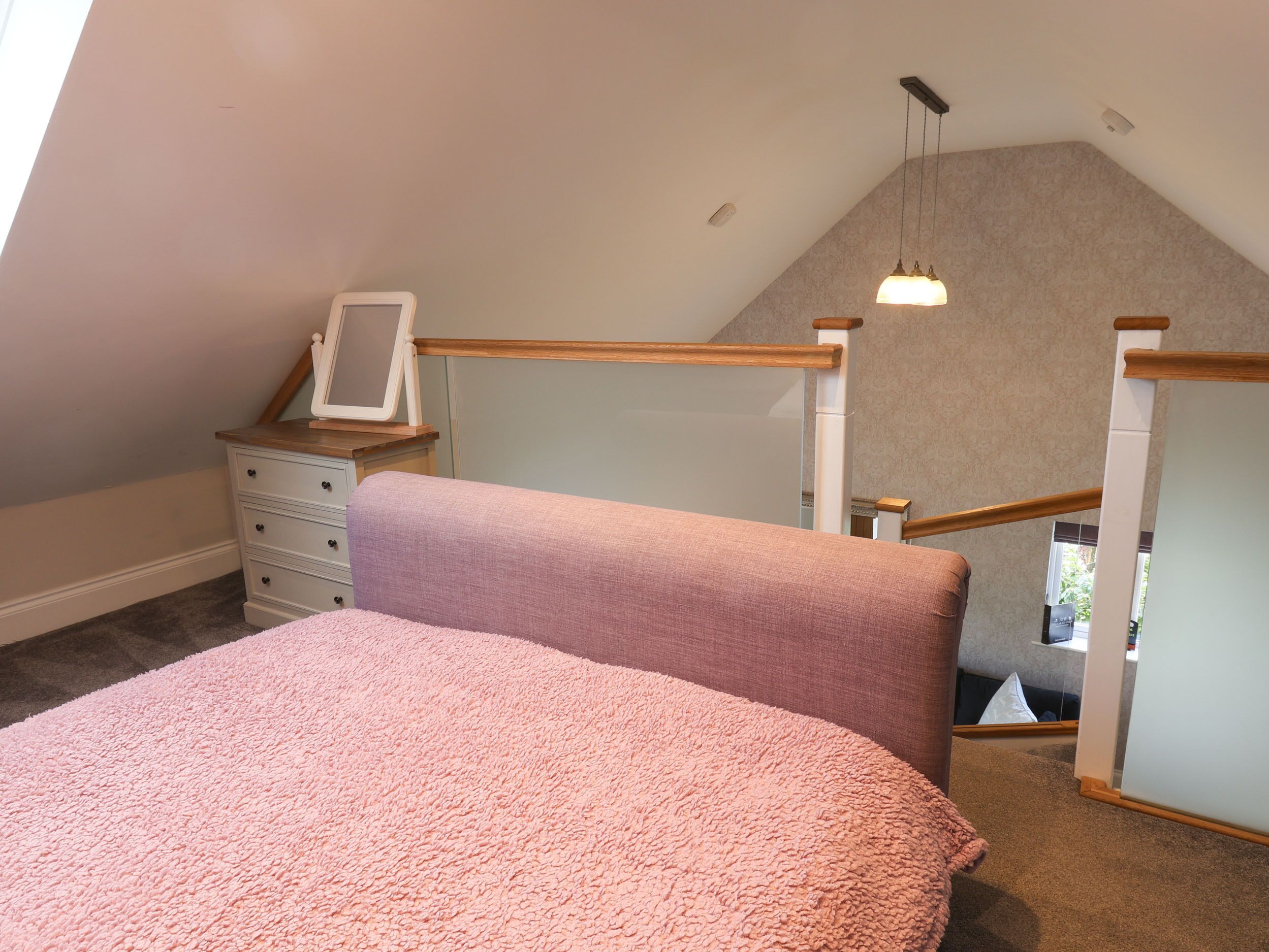 A bedroom with a bed, a dresser, a mirror, and a staircase leading to an upper level.