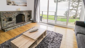 Un soggiorno con camino in pietra, un tavolino in legno e vista sull'esterno attraverso ampie porte vetrate.