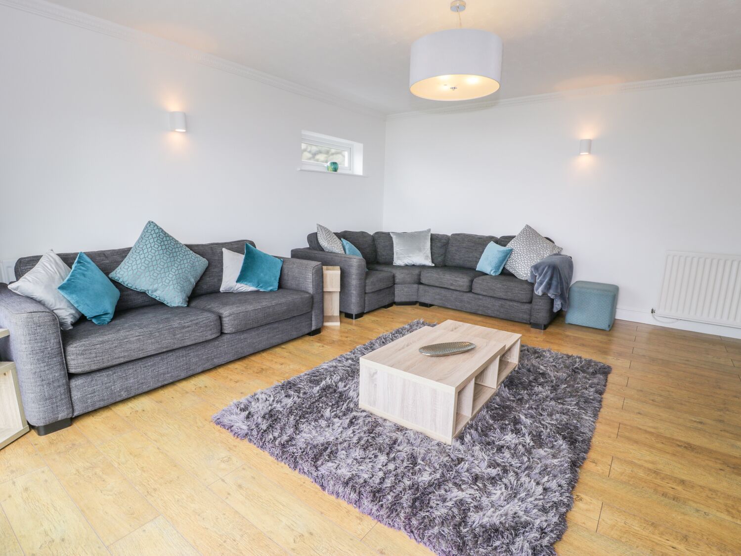 A modern living room with two grey sofas, a wooden coffee table, and a fluffy grey rug.