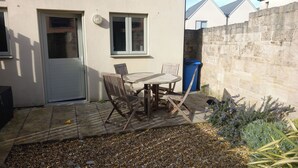 A patio with a table and chairs, a door, windows, a stone wall, and a blue trash bin. - Olympic Cottage (Portland)