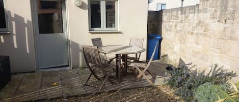 A patio with a table and chairs, a door, windows, a stone wall, and a blue trash bin.