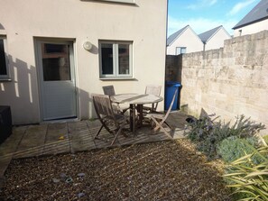 A patio with a table and chairs, a door, windows, a stone wall, and a blue trash bin. - Olympic Cottage (Portland)
