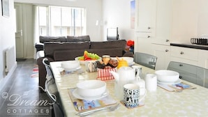 Un salon moderne avec un canapé, une table à manger dressée avec des assiettes, des tasses et un saladier rempli de fruits.