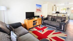 A living room with a sofa, a TV, a wooden cabinet, and a kitchen in the background. - Olympic Cottage (Portland)