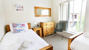 Ein Schlafzimmer mit zwei Betten, einer Holzkommode, einem Stuhl, einem Spiegel und einem Fenster mit Jalousien.