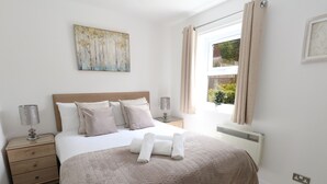 Une chambre bien rangée, avec un grand lit, des tables de chevet, un radiateur et une fenêtre avec des rideaux.