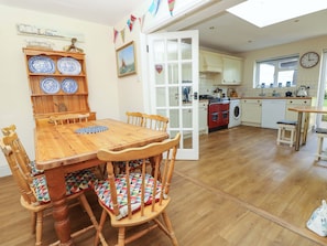 A dining area with a wooden table and chairs, a kitchen with appliances, and a view of the outside. - Tovah (Yarmouth)