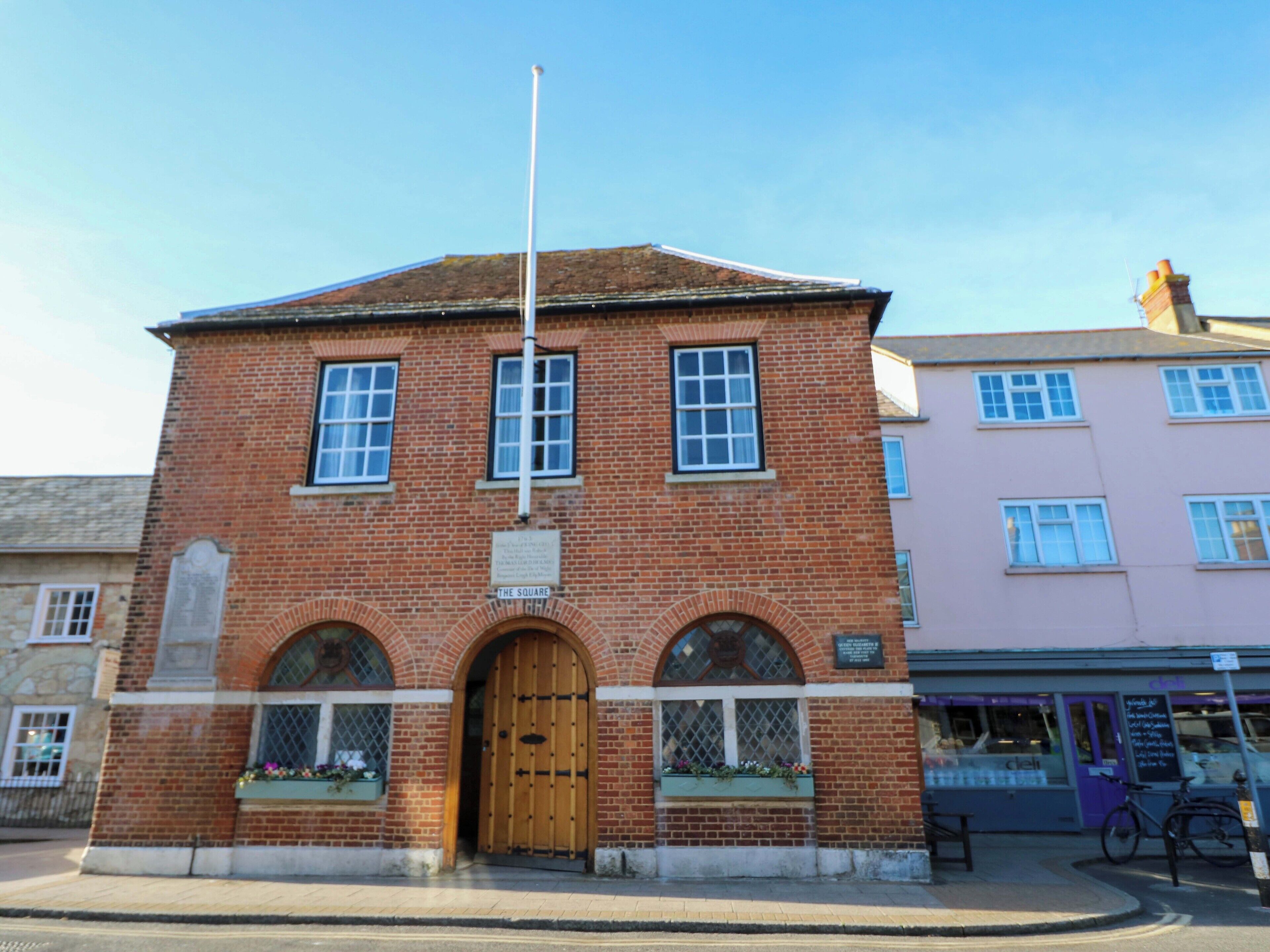 A brick building with a central arched entrance, a flagpole, and a sign reading 'The Square.'