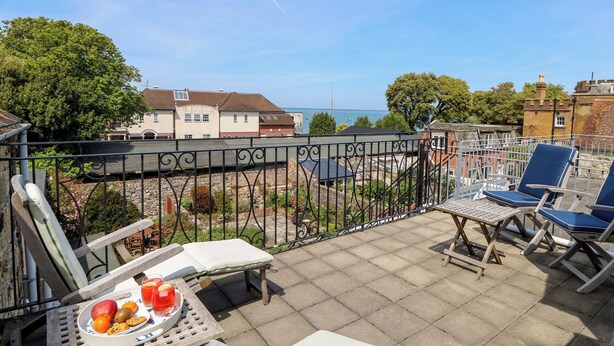 En balkon med et bord dækket til to personer, en stol og udsigt over havet og bygninger.