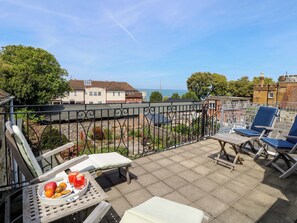 Ein Balkon mit Tisch fĂŒr zwei Personen, einem Stuhl und Blick auf das Meer und die GebĂ€ude.