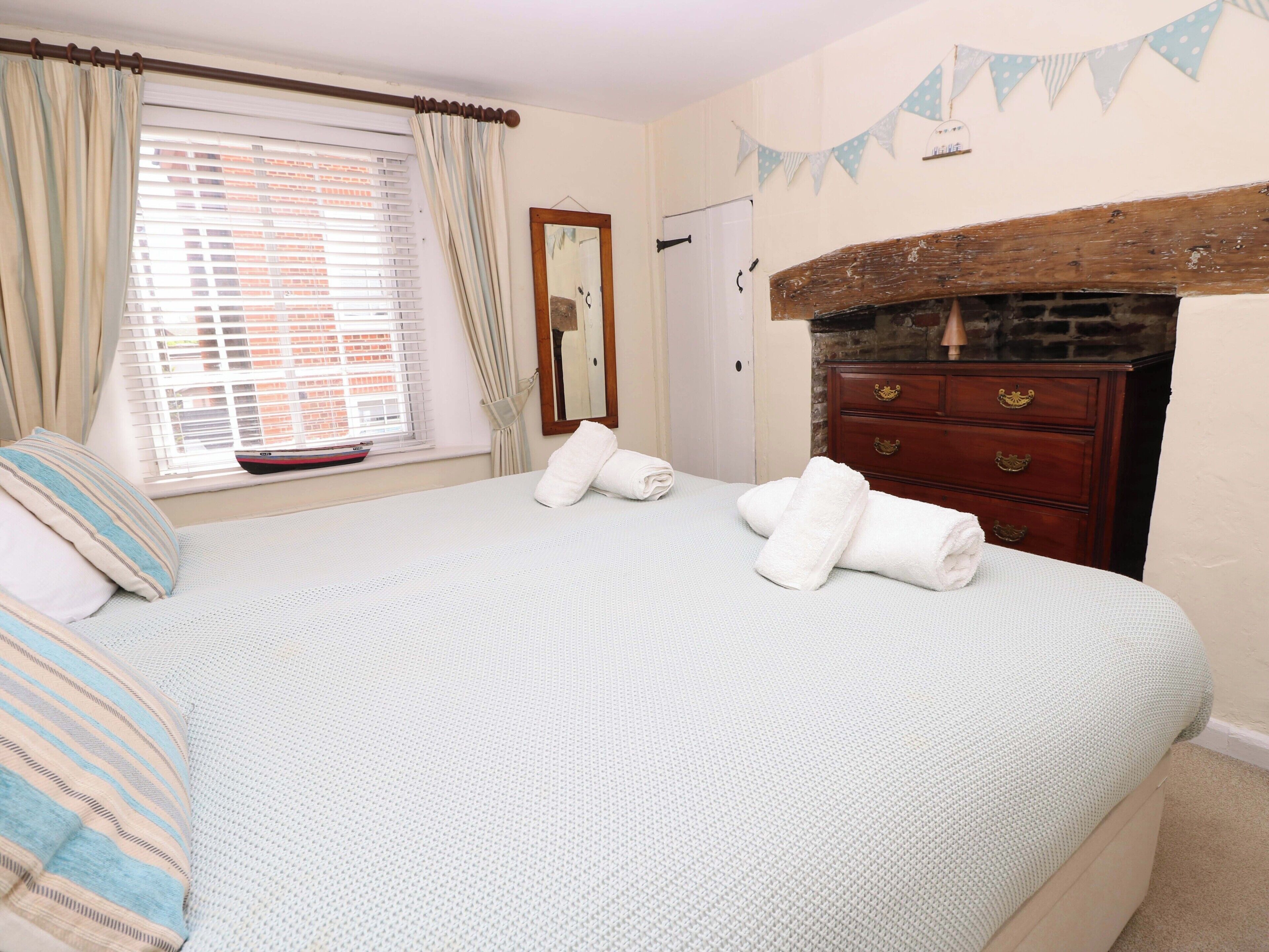 Un dormitorio con cama, cómoda, espejo y ventana con cortinas.
