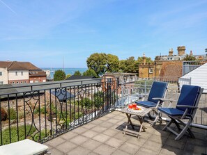Ein Balkon mit Tisch, StĂŒhlen und Blick auf das Meer und die GebĂ€ude.