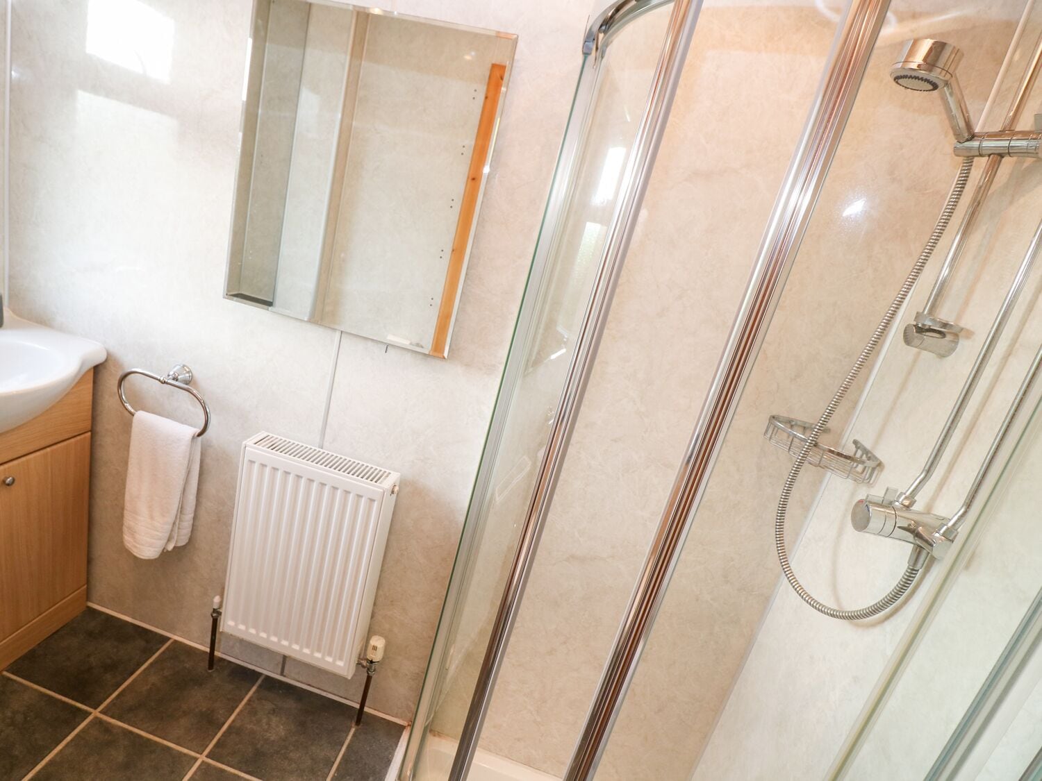 A modern bathroom with a glass shower enclosure, a white radiator, and a wooden cabinet.