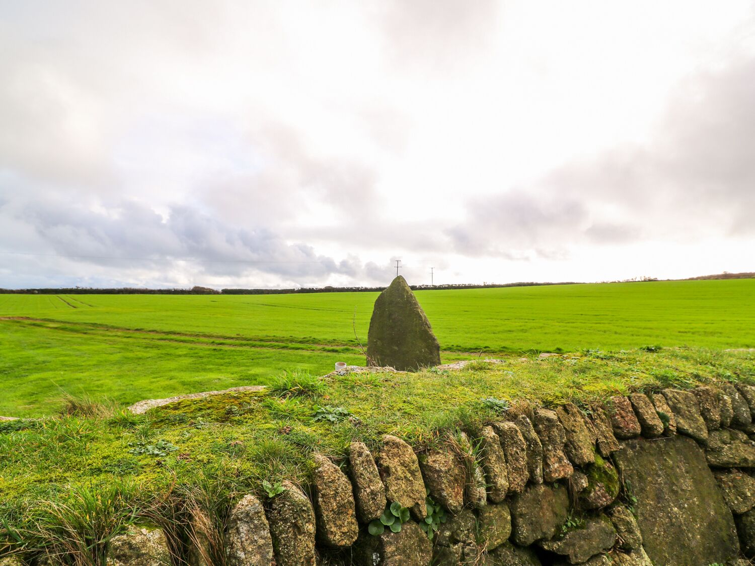 Un mur de pierres, un champ verdoyant et, au loin, un monument en pierre.