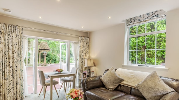 A living room with a leather sofa, a coffee table, a dining table with chairs, and a large window with a view of greenery. - Silvadale Cottage (Louth)