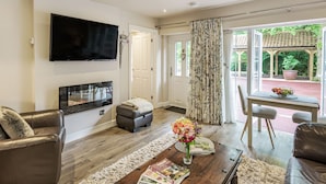 A living room with a flat-screen TV, a fireplace, a coffee table with magazines, and a view of a garden through the glass door. - Silvadale Cottage (Louth)
