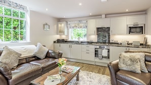 A modern kitchen with white cabinets, a black countertop, and stainless steel appliances. There is a window with a view of greenery outside. - Silvadale Cottage (Louth)