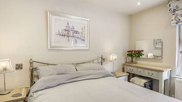 A neatly arranged bedroom with a bed, bedside tables, a nightstand, a dresser, a mirror, and a framed picture on the wall.