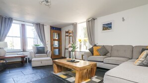 A modern living room with a sofa, a wooden coffee table, and a dining table. - Miner's Rest (Camborne)