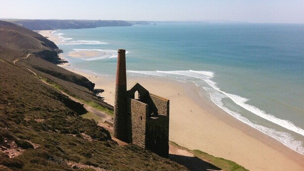 A coastal landscape with a prominent stone structure, a sandy beach, and a clear view of the ocean. - Miner's Rest (Camborne)