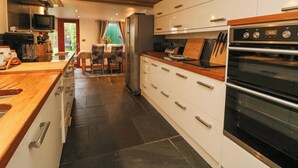 A modern kitchen with a built-in oven, stainless steel appliances, and a wooden countertop. - Miner's Rest (Camborne)