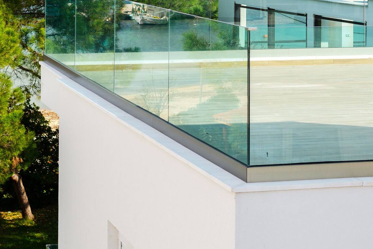 Un bâtiment moderne doté d’un balcon en verre donnant sur une étendue d’eau et un paysage vallonné.