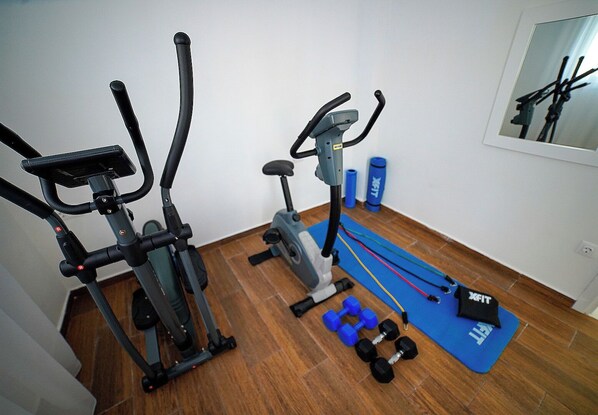 Un gimnasio en casa con dos bicicletas estáticas, una máquina de remo y una colchoneta azul con mancuernas.