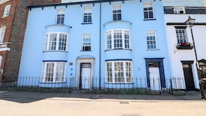 A two-story building with a blue facade, multiple windows, and a black metal fence in front. - Tradewinds (Weymouth)
