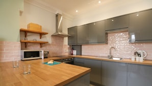 A modern kitchen with a wooden countertop, stainless steel appliances, and grey cabinetry. - Tradewinds (Weymouth)