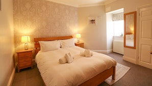 A neatly made bed with two pillows, a bedside table with a lamp, and a mirror on the wall. - Tradewinds (Weymouth)