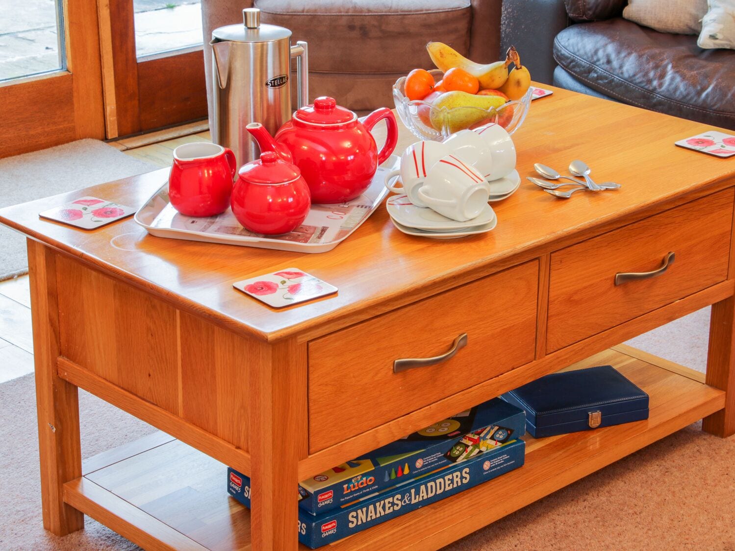 A wooden table with a tray of red teapots, white cups, and a fruit bowl.
