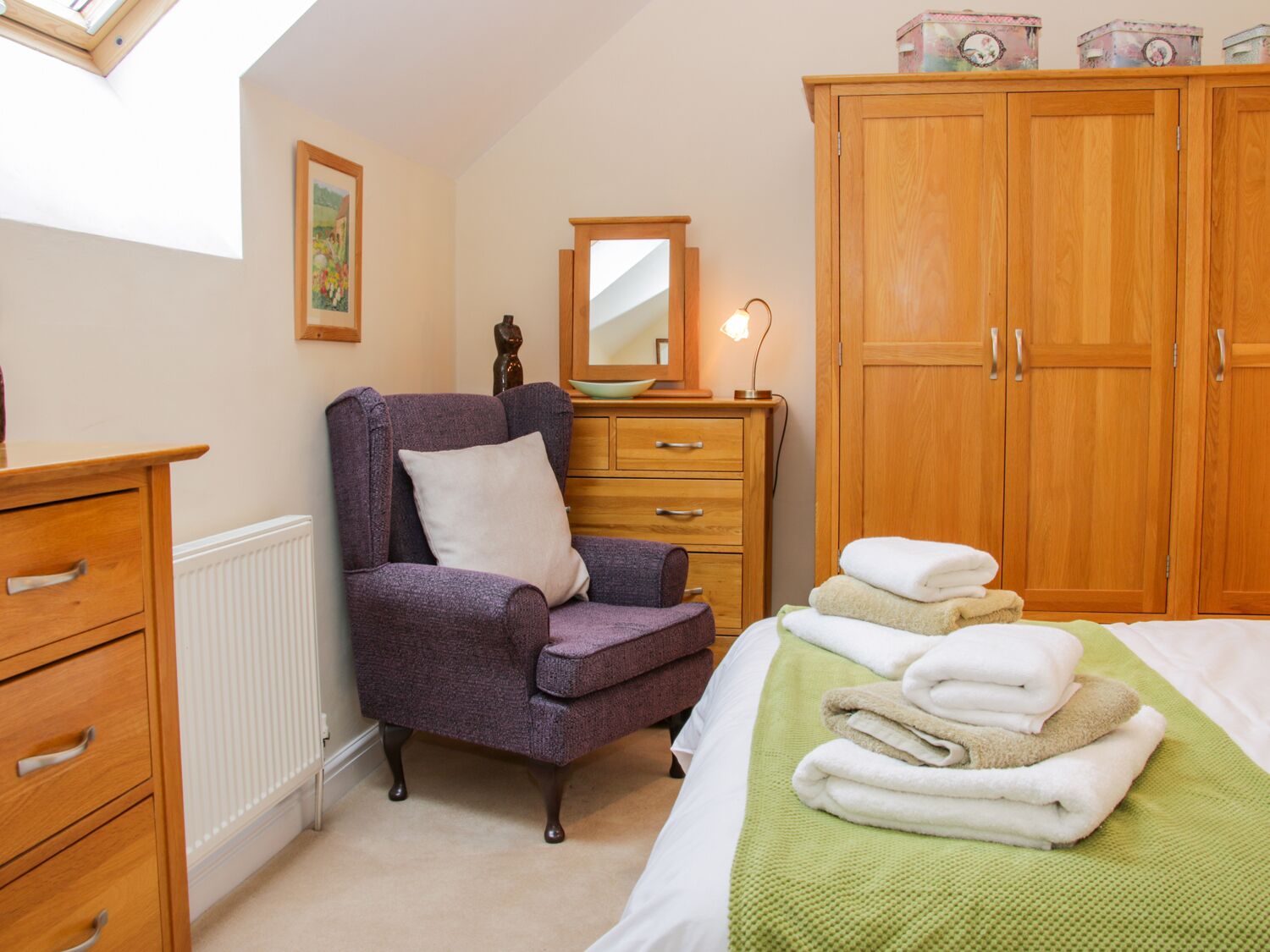 Een slaapkamer met een paarse fauteuil, een houten dressoir, een spiegel en een garderobe.