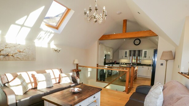 A spacious living room with a wooden coffee table, a sofa, and a glass railing leading to a kitchen. - Bwthyn Carregwen (Penmaenmawr)