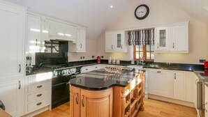 A spacious kitchen with white cabinets, a black countertop, and a wooden island. - Bwthyn Carregwen (Penmaenmawr)