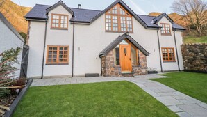 A two-story house with a stone facade, a wooden front door, and a well-maintained lawn. - Bwthyn Carregwen (Penmaenmawr)