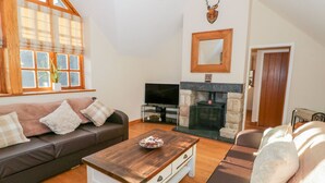 A cozy living room with a sofa, a coffee table, a fireplace, and a television. - Bwthyn Carregwen (Penmaenmawr)