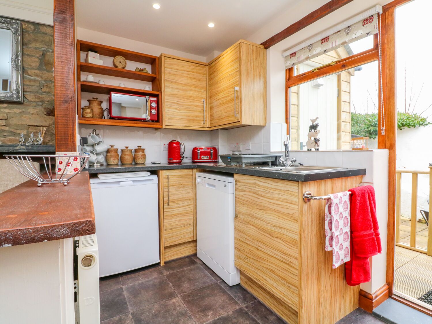 Eine kompakte Küche mit Holzausstattung, einer Mikrowelle, einem Toaster und einem Geschirrspüler.