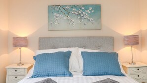 Un lit bien fait, avec une literie bleue et blanche, deux tables de chevet avec des lampes et un tableau représentant des fleurs accroché au mur.