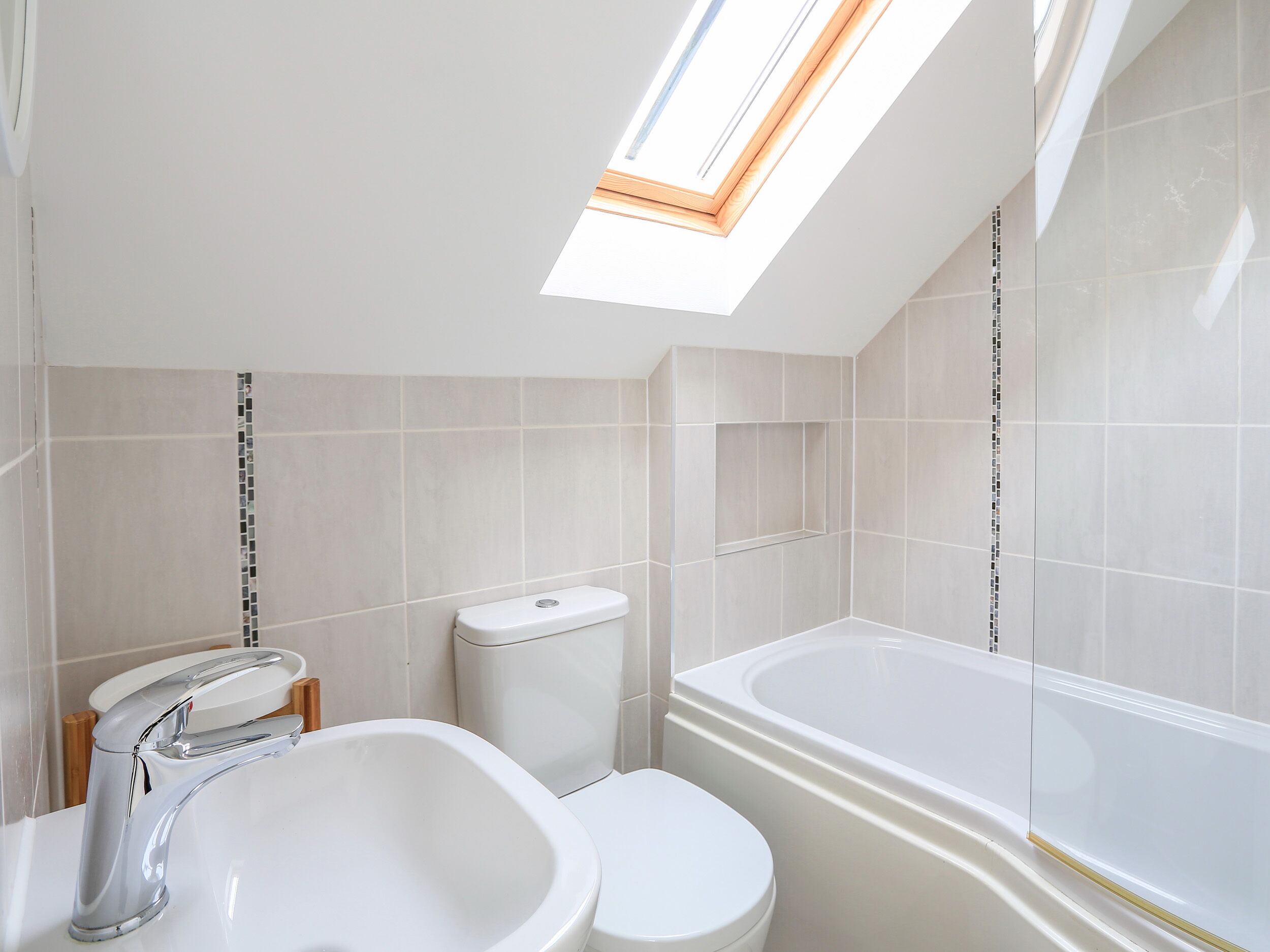 A modern bathroom with a skylight, a sink, toilet, and bathtub.