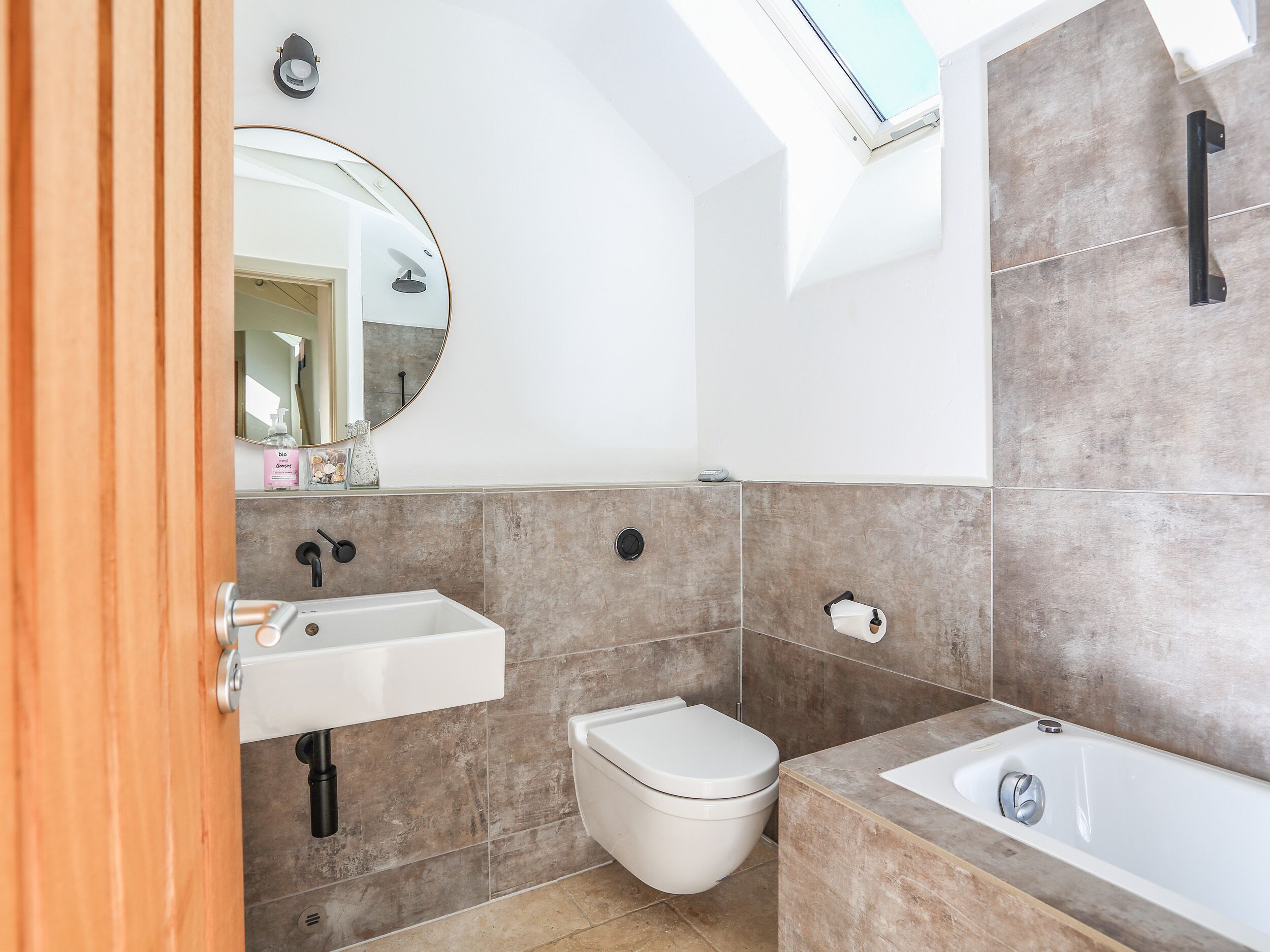 A modern bathroom with a skylight, a white sink, a toilet, and a bathtub.