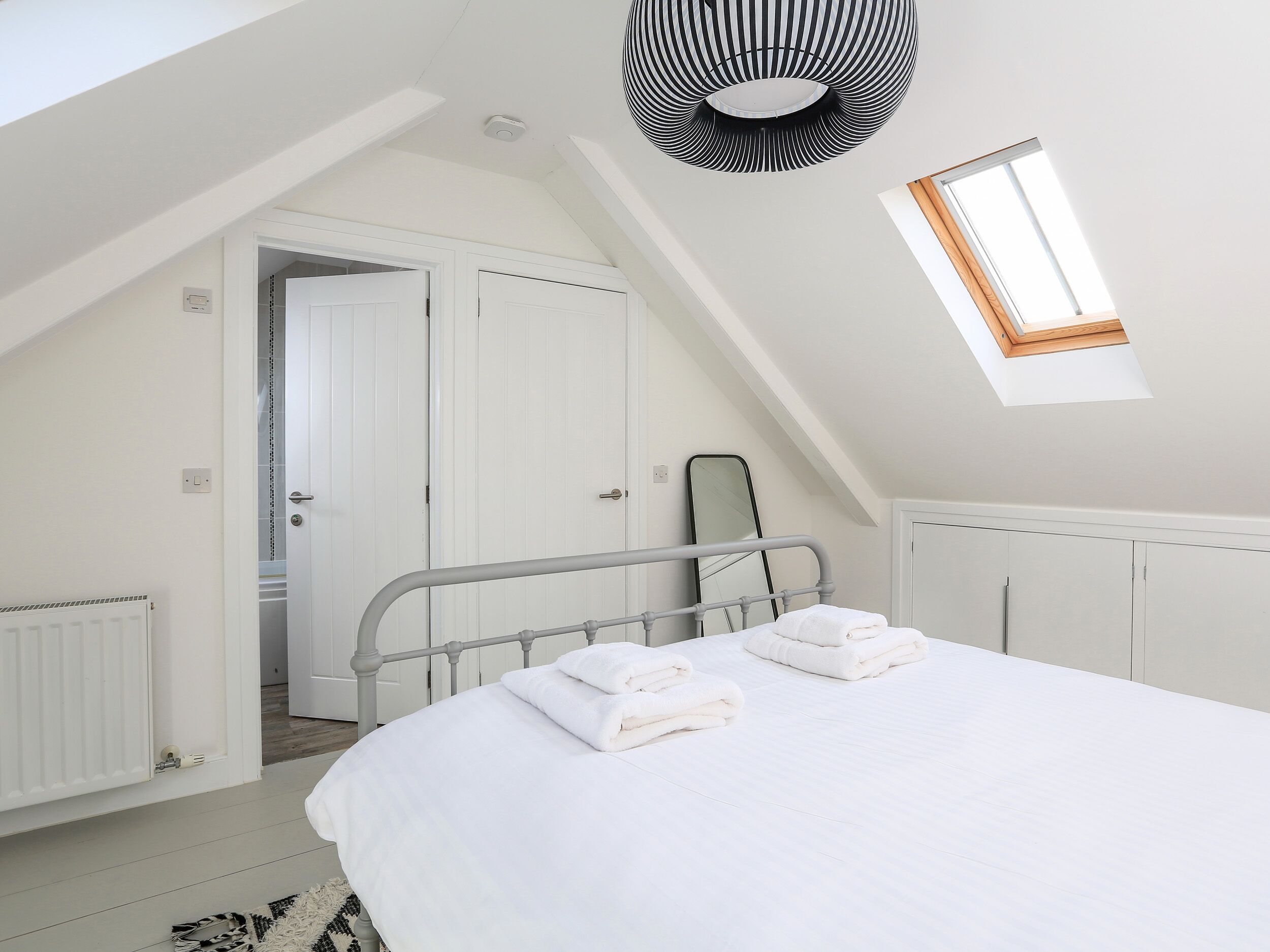 A bedroom with a sloped ceiling, a skylight, a bed with white linens, a radiator, and a wardrobe.