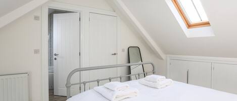 A bedroom with a sloped ceiling, a skylight, a bed with white linens, a radiator, and a wardrobe.