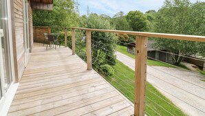Una terraza de madera con barandilla, con vistas a un paisaje verde y un camino de grava.