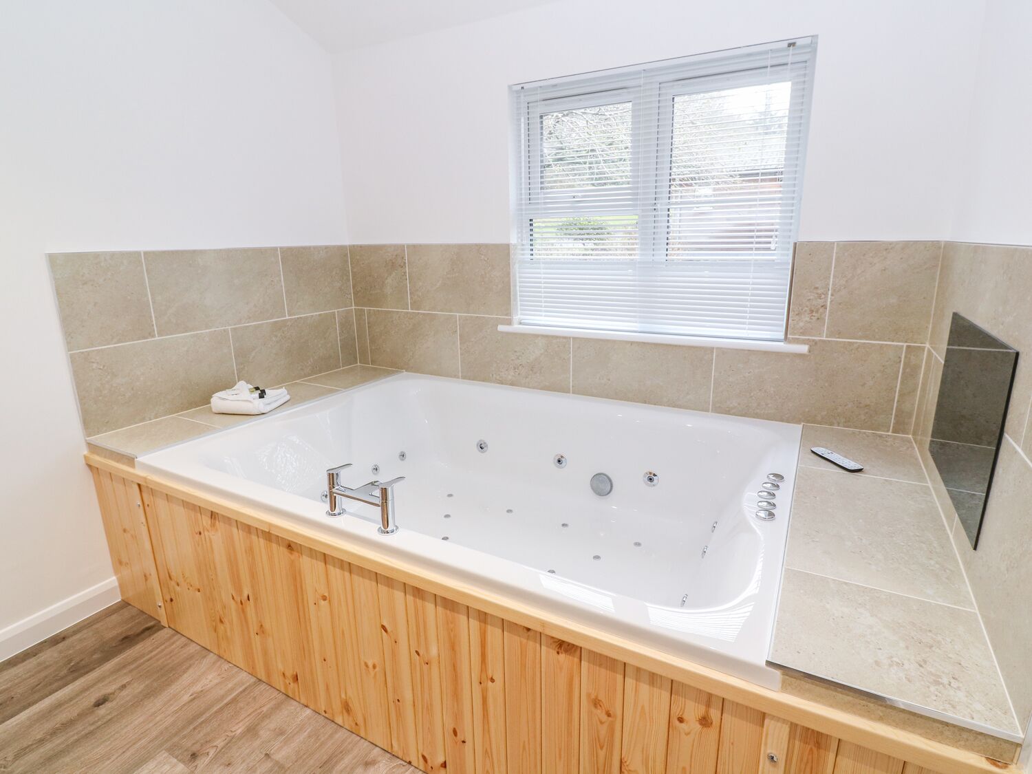 A modern bathroom with a freestanding bathtub, wooden flooring, and beige tiles.